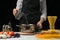 The chef pours water into the pan, on a black background, with pasta on the table, vegetables and spaghetti, mushrooms. The concep
