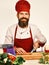Chef prepares meal. Professional cookery concept. Man with beard cuts carrot with knife on white background. Cook with