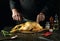 The chef prepares to cut a raw rooster with a knife on a kitchen cutting board. Cooking cockerel with fragrant spices and rosemary