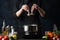 The chef in professional uniform adding seafood to the traditional asian dish in steaming pot. Spices, fruits, vegetables are on