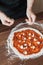 Chef puts cheese on dough with tomato paste on pizza
