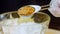 The chef puts the granulated mustard in a transparent bowl decorated with squares on the table with a spoon. Slider and