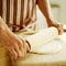 Chef rolling out pizza dough with a wooden rolling pin wearing a red stripy apron. Conceptual image