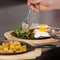 Chef\'s Hand Pouring Sauce On Egg Dish In Kitchen