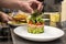 Chef\'s hands finishing assembling a salmon tartare with avocado and chopped cherry tomatoes on the metal kitchen table