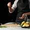 Chef salting mackerel fish on a black background