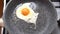 Chef seasons a Frying egg, sunny side up, with ground pepper in a small frying pan over an gas burning stove