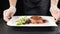 Chef serving dish. Close up shot of chef hands putting a plate with steak and green salad on table. hd. in Luxury