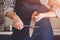 A chef in a shirt and apron stands in the kitchen sharpening the blade of a steel knife