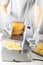 A chef is slicing a large chunk of swiss cheese using an electrical deli slicer.