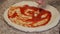 Chef spreading tomato sauce on pizza dough