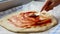 Chef spreading tomato sauce on pizza dough with a spoon in kitchen