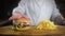 Chef squeezes juicy delicious burger and sauce drips from it in slow motion, cooking burgers and fries at the fast food