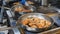 The chef turns over the two scapulars meat that is fried in two frying pans in the kitchen of the restaurant, the meat