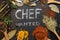 Chef wanted written on black stone tile with white chalk, surrounded by condiments an kitchen tools