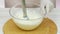 Chef whipping cream with a blender in a glass bowl. Hand in white glove. White wooden table.