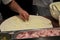 The chef in a white apron makes a huge pizza, close-up of pizza ingredients-ham, cheese, Dark background