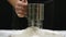 A chefs hand sifts flour through a sieve on a black background. Baking preparation, sift flour.