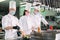 Chefs in protective masks and gloves prepare food in the kitchen of a restaurant or hotel.