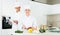 Chefs in uniform prepare vegetables with paper recipe on kitchen