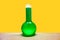 Chemical retort glass bottle with poisoned green liquid on yellow wall background