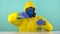 A chemical technician in a protective yellow suit, gloves and glasses pours from one flask from a blue chemical liquid