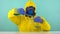 A chemical technician in a protective yellow suit, gloves and glasses pours from one flask with chemical elements to