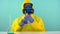 A chemical technician in a protective yellow suit, gloves and glasses is trying to drink a blue chemical liquid from a