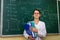 Chemist with folders standing and posing for camera. Behind woman university board with chemical formulas