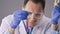 Chemist in glasses oversees process of mixing chemicals in test tubes