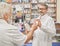 Chemist offering medicaments to old customer in pharmacy.