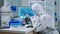 Chemist in protection suit typing on pc and analyzing virus sample