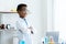 .In chemistry classroom with many laboratory tools. A young African boy in white lab coat and safety glasses stand with arms
