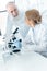 Chemists in white uniform working with microscope and looking at each other in laboratory