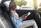 Cherful Black Woman In Hijab Using Digital Tablet On Backseat In Car