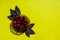 Cherries in a glass bowl on a yellow background with basil leaves