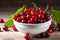 Cherries with leaves glisten in a white bowl on wooden backdrop