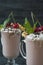 Cherry milkshake with ice cream and whipped cream, marshmallows, cookies, waffles, served in a glass cup. Dark wooden background