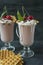 Cherry milkshake with ice cream and whipped cream, marshmallows, cookies, waffles, served in a glass cup. Dark wooden background