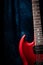 Cherry red electric guitar standing upright with a dark blue background and moody lighting