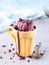 Cherry red ice cream in a regular yellow mug and spoon, on a blue background, with topping and crumbs. Unusual serve of dessert,