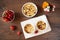 Cherry, strawberry crumble dessert in white bowls. Cherries, strawberries, flowers behind. Dark wood background, top view