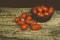 Cherry tomatoes in an African ebony wood bowl on a wooden surface with a black background. Some cherry are fallen on the table.