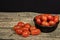 Cherry tomatoes in an African ebony wood bowl on a wooden surface with a black background. Some cherry are fallen on the table.