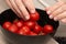 Cherry Tomatoes in a bowl in female hands. Hands cradling a black bowl filled with bright red cherry tomatoes