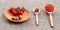 Cherry tomatoes in a wooden plate on a gray background. Food background. Adjika sauce, red and black pepper in spoons on burlap.