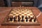 Chess board with figures on brown marble table. Beginning of game.