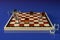 Chess Board with glasses of alcoholic beverages, instead of checkers. On a blue background. Alcoholic drinks in shot glasses as