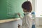 Chess lesson for children. Boy draws a chessboard on the green board in the classroom.