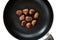 Chestnut on a black frying pan isolated on white background, top view. Roasted Chestnuts close up